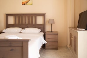 Un dormitorio con una cama de madera, una mesita de noche con una lámpara y un televisor sobre un mueble.
