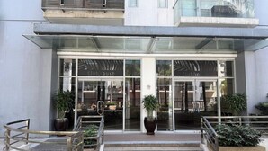 A hotel entrance with glass doors, outdoor seating, and potted plants.