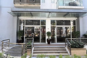 A hotel entrance with glass doors, outdoor seating, and potted plants.
