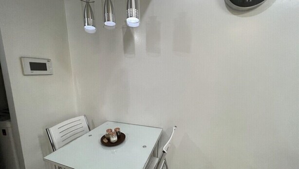 A dining area with a white table, metal chairs, a clock on the wall, and pendant lights.