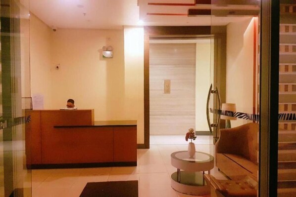 A reception area with a reception desk, a sofa, a small table with a vase, and a door leading to another room. - Dels Condotel by Zuzu (Pasay)