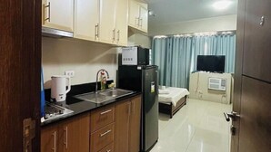 A compact hotel room with a kitchenette, a bed, a TV, and a small bathroom.
