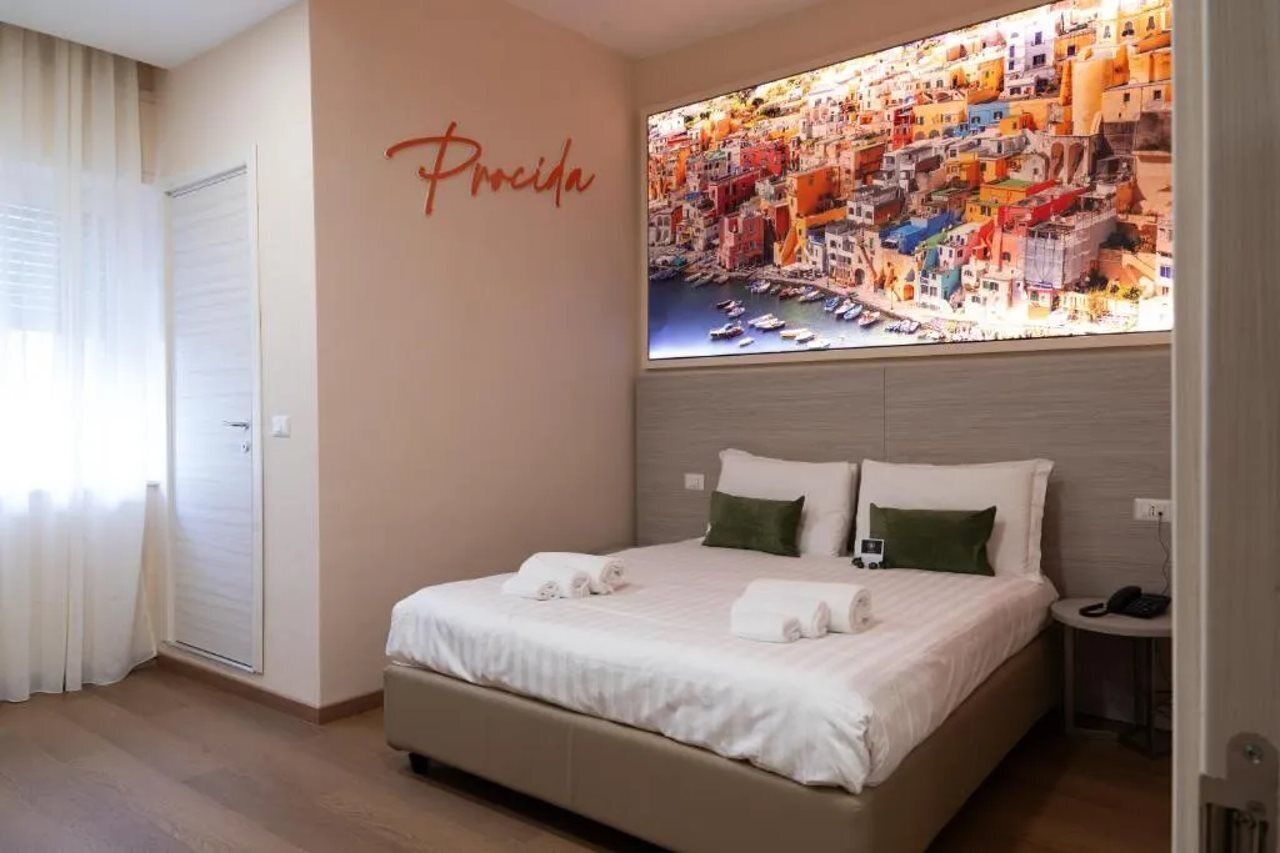 A hotel room with a bed, pillows, a nightstand, a telephone, and a wall with a cityscape picture.