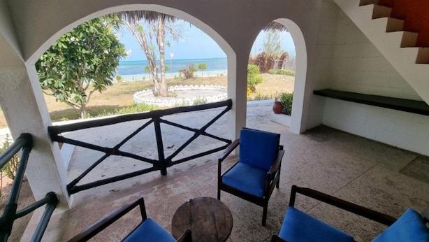 A covered outdoor seating area with blue chairs and a table, overlooking a beach and palm trees. - F-zeen Boutique Hotel Zanzibar (Uroa)
