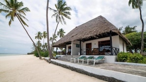 A beachfront property with a thatched-roof building, a sandy beach, and palm trees. - F-zeen Boutique Hotel Zanzibar (Uroa)
