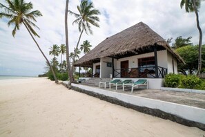 A beachfront property with a thatched-roof building, a sandy beach, and palm trees. - F-zeen Boutique Hotel Zanzibar (Uroa)