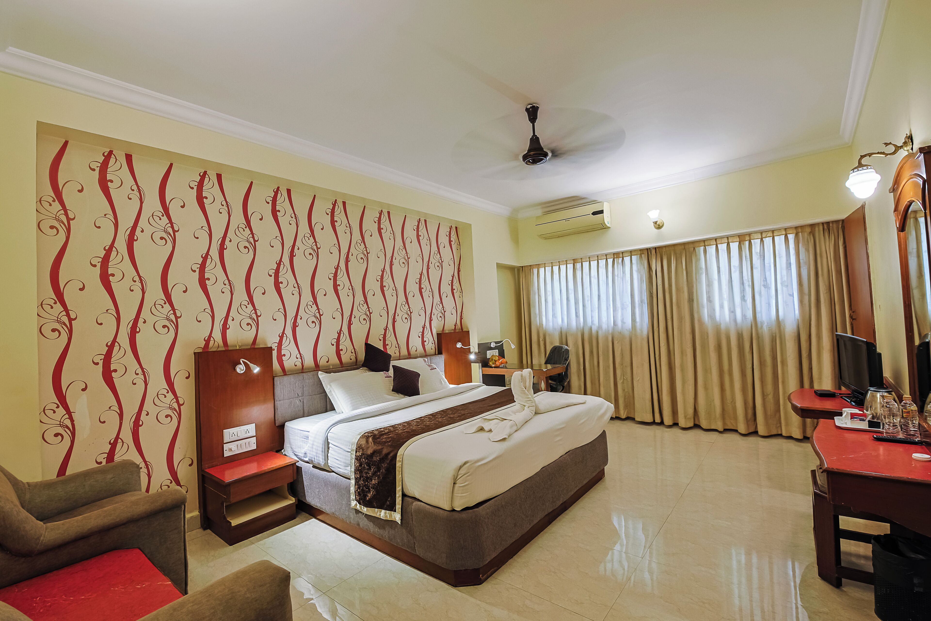 A hotel room with a bed, a desk, a chair, a TV, and a ceiling fan.