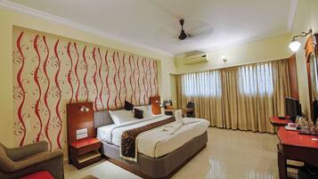 A hotel room with a bed, a desk, a chair, a TV, and a ceiling fan.
