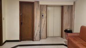 A hallway with a wooden door, a marble wall, and a red-striped chair. - Hotel Maruya Palace (Mysore)