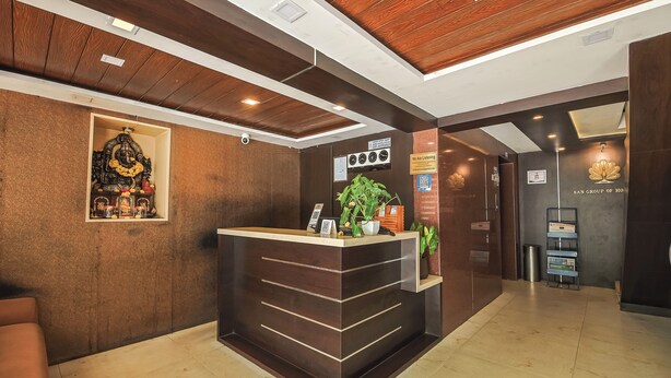 A reception desk with a clock, a sign indicating a listening service, and a plant. - Hotel Maruya Palace (Mysore)