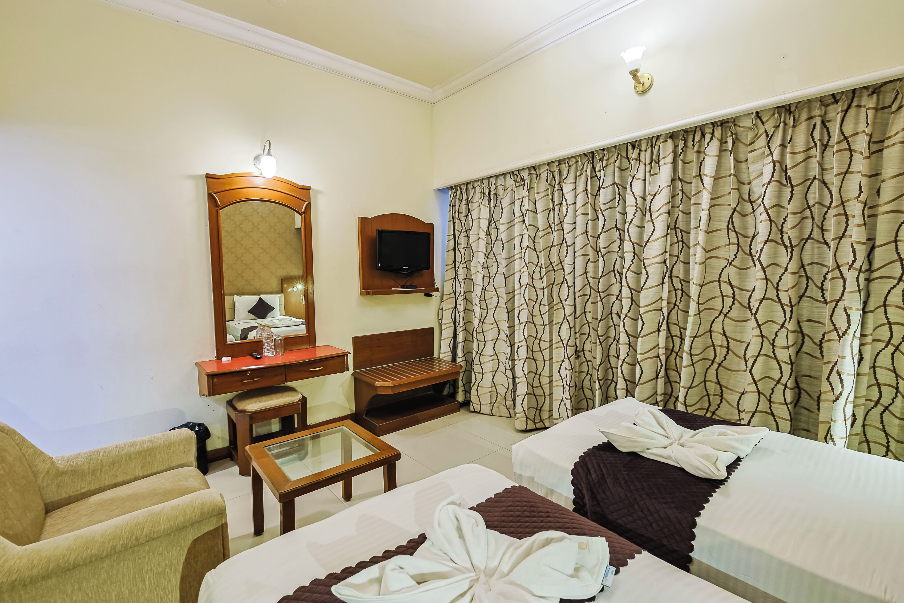 Habitación de hotel con cama, escritorio, silla, televisor y un ventanal con cortinas.