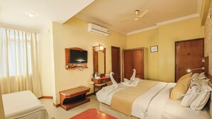A hotel room with a bed, a desk, a chair, a television, and an air conditioning unit. - Hotel Maruya Palace (Mysore)