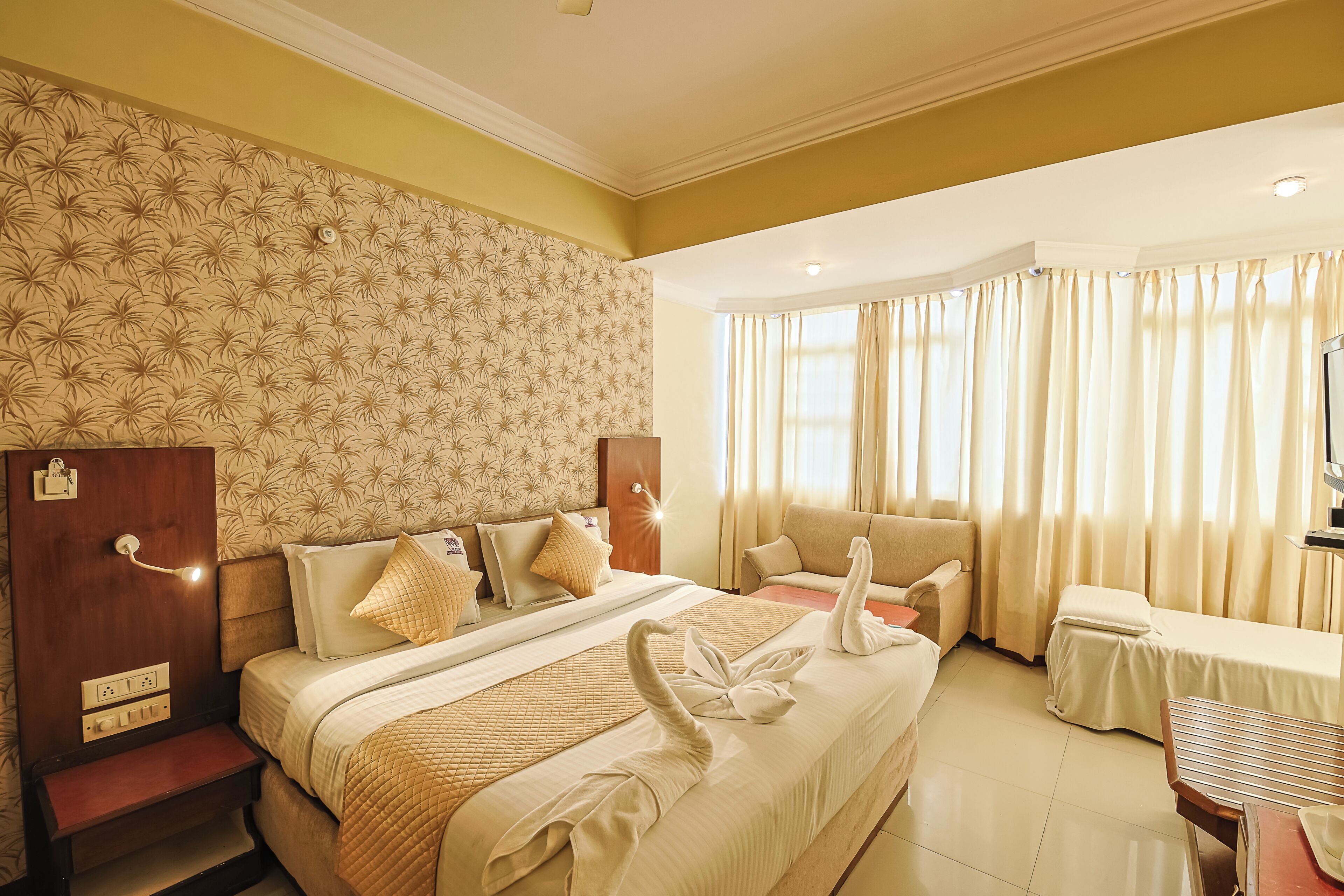 A hotel room with a large bed, a sofa, a desk, and a television.