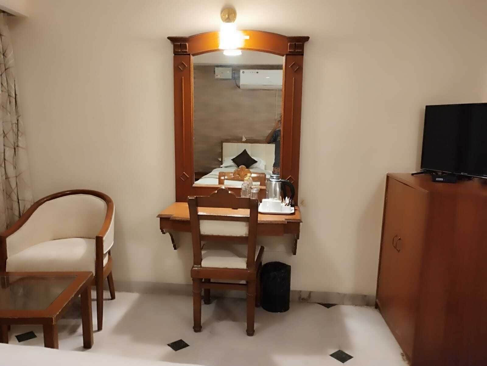 A hotel room with a wooden desk, a chair, a television, and a mirror.