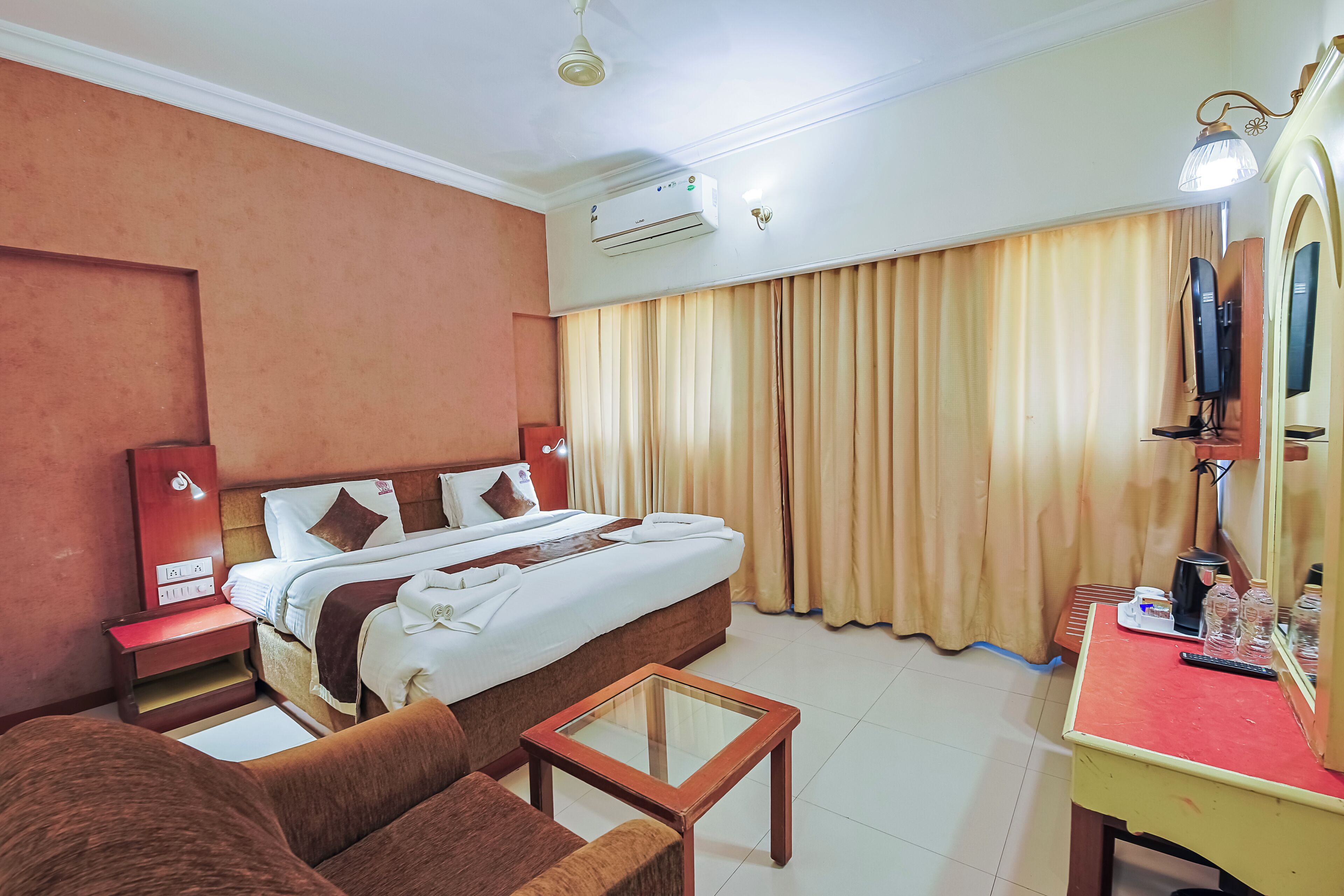 A hotel room with a bed, a desk, a chair, a mirror, and a television.