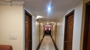 A hotel corridor with doors on both sides, a tiled floor, and a light fixture on the ceiling. - Hotel Maruya Palace (Mysore)