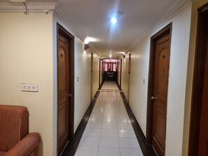 A hotel corridor with doors on both sides, a tiled floor, and a light fixture on the ceiling.