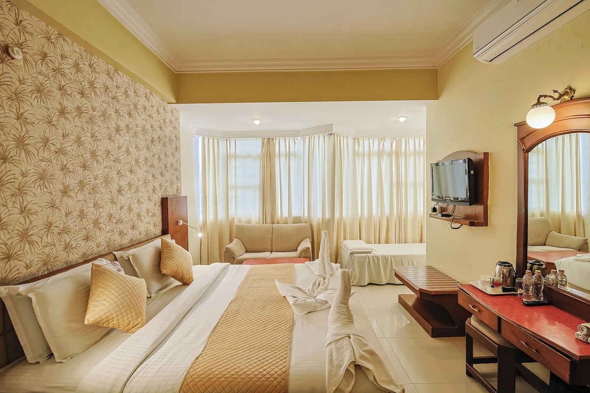 A hotel room with a large bed, a sofa, a desk, and a television.