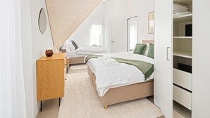 A bedroom with a bed, a wooden dresser, a closet, and a slanted ceiling.