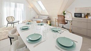 A modern dining area with a long table set for four, a sofa, a TV, and a kitchen area.
