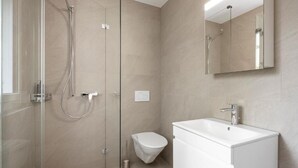 A modern bathroom with a glass-enclosed shower, a toilet, and a white sink with a mirror above it.