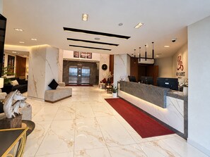 A hotel lobby with a reception desk, seating area, and elevators.