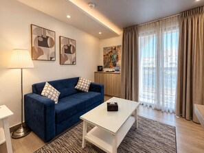 Una sala de estar moderna con un sofá azul, una mesa de centro blanca y una lámpara de pie. Hay pinturas abstractas en la pared y una obra de arte colorida sobre el sofá.