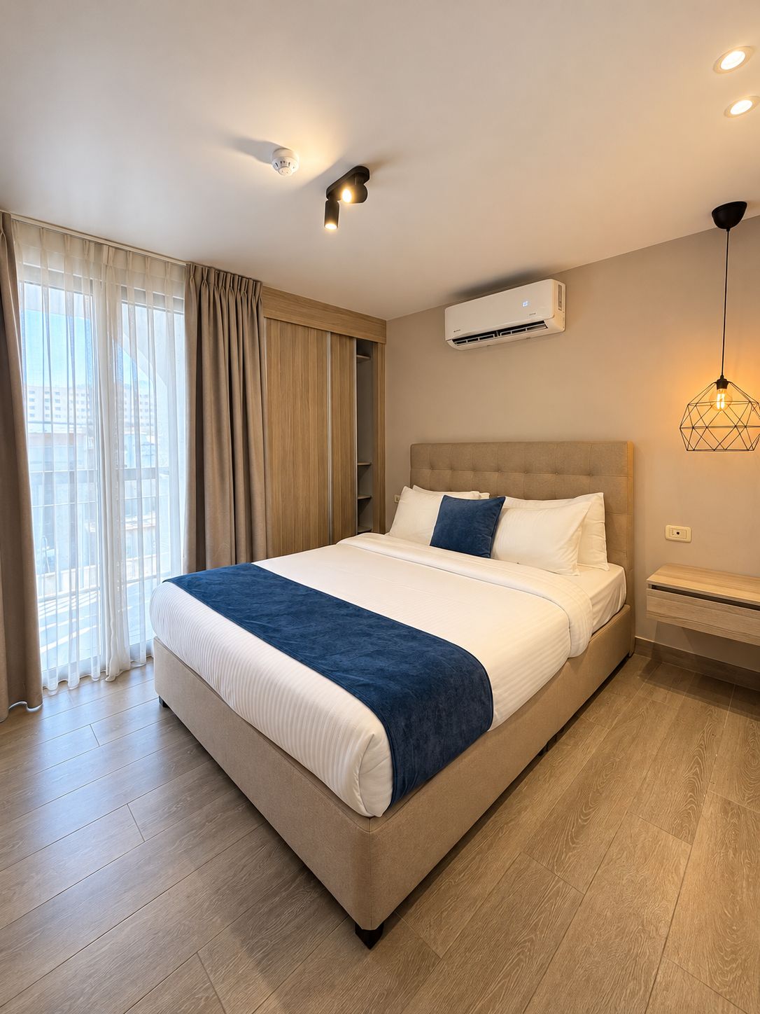 Une chambre d’hôtel avec un lit, un appareil de climatisation, un luminaire suspendu et une vue par la fenêtre.