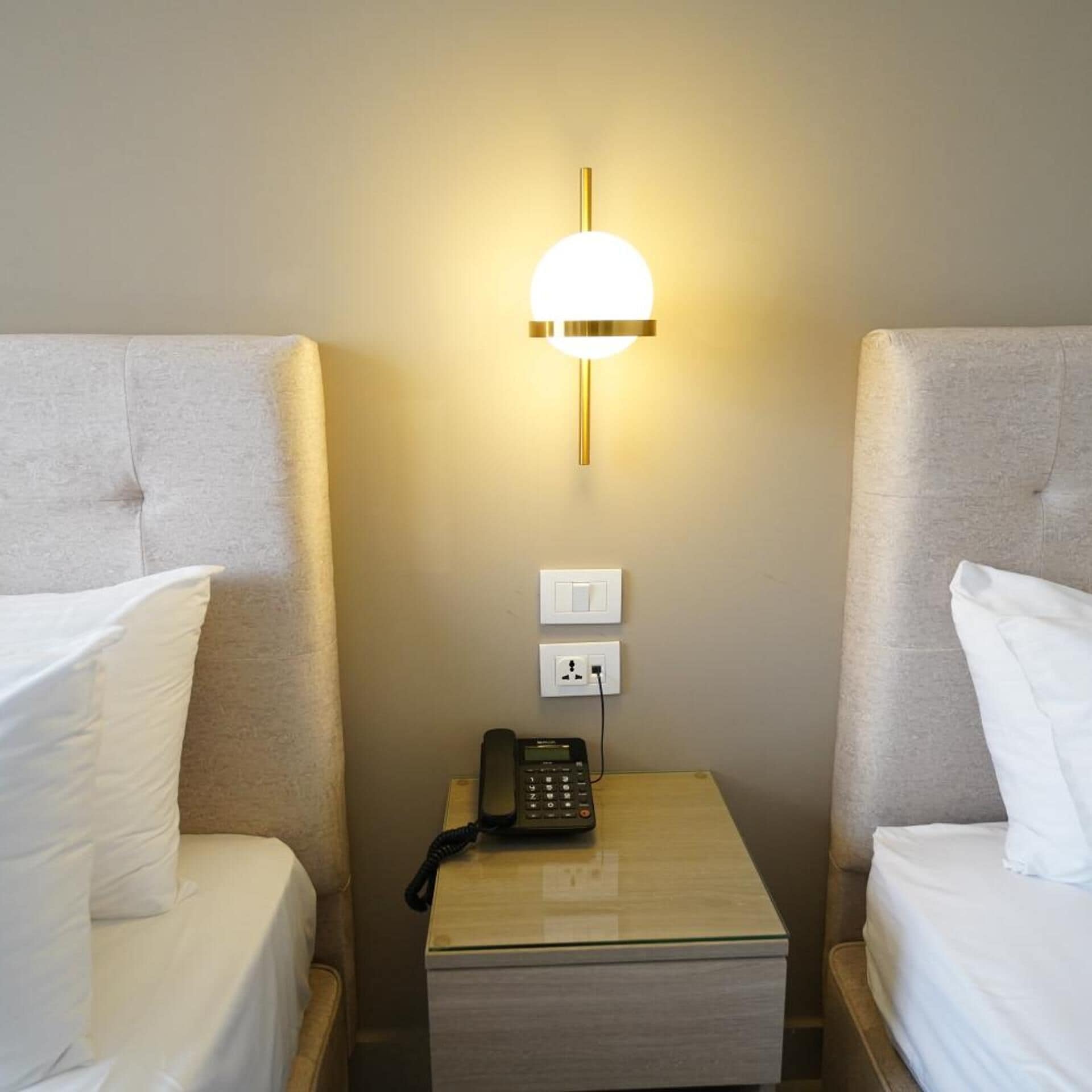 Ein Hotelzimmer mit zwei Betten, einem Nachttisch mit Telefon und einer Wandleuchte.