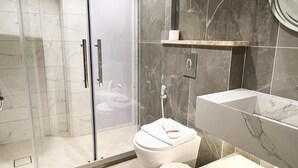 A modern bathroom with a glass-enclosed shower, a white toilet, a vanity with a mirror, and a towel rack. - Red Carpet Hotel & Suite (Amman)