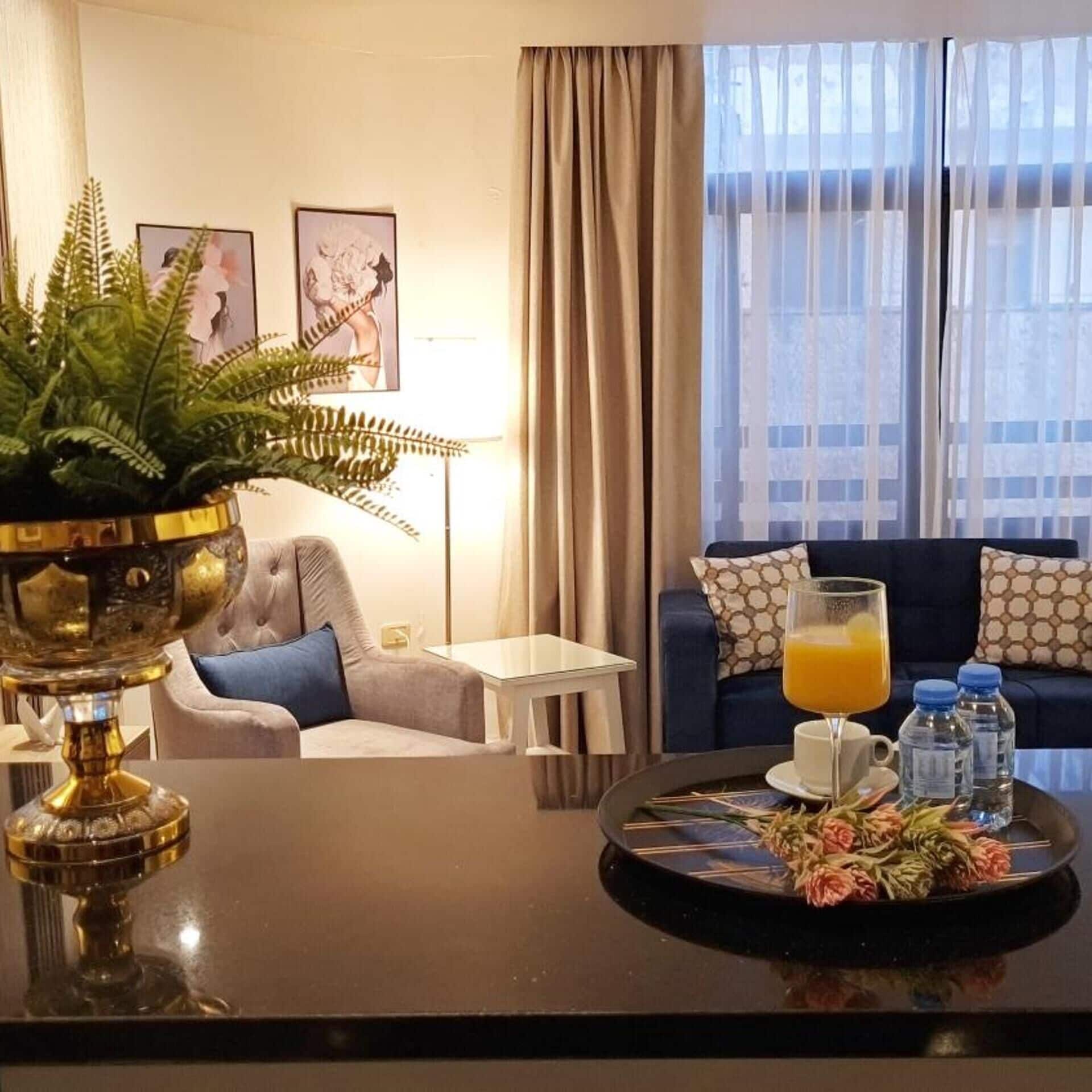 Ein Hotelzimmer mit Esstisch, einer Couch, einem Blumentopf und einem Fenster mit Vorhängen.