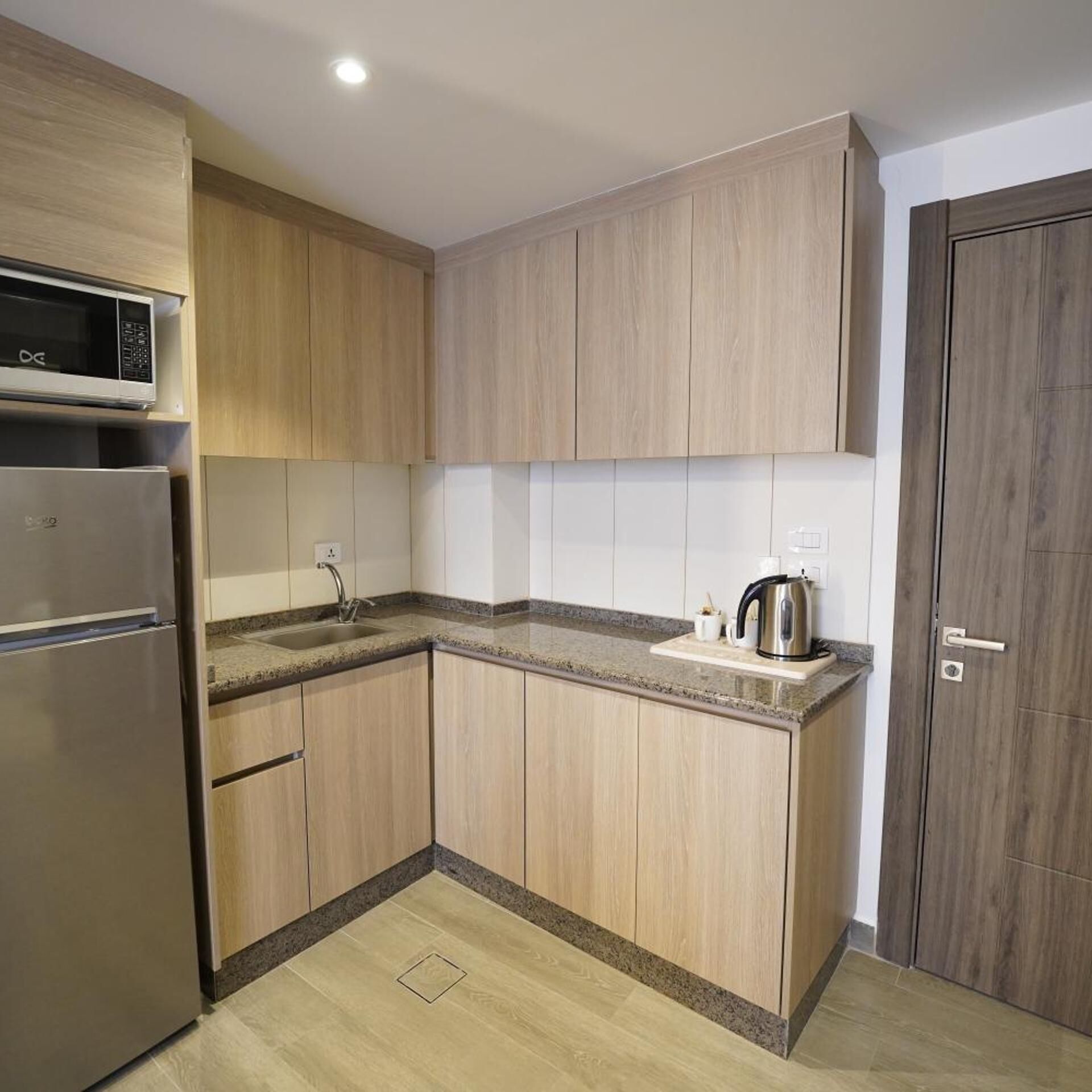 A kitchen with wooden cabinets, a stainless steel refrigerator, a microwave, a sink, and a kettle.