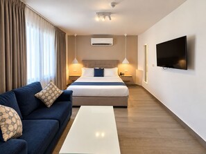 A hotel room with a bed, a sofa, a TV, and a ceiling-mounted air conditioning unit.