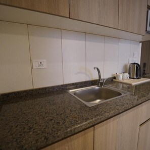 A kitchen with a granite countertop, stainless steel sink, and wooden cabinets. - Red Carpet Hotel & Suite (Amman)