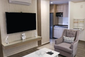 A modern living room with a flat-screen TV, a glass coffee table, a comfortable armchair, and a kitchen area in the background. - Red Carpet Hotel & Suite (Amman)