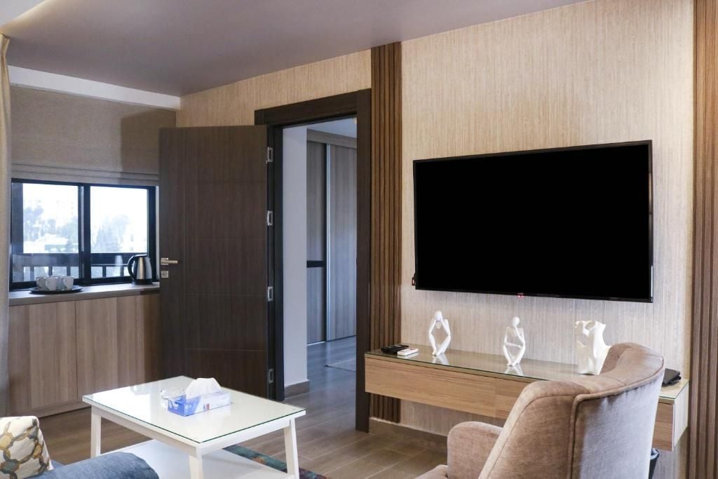 A modern living room with a flat-screen TV, a glass coffee table, and a sofa.