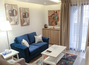 A living room with a blue sofa, a white coffee table, and a painting of a zebra on the wall. - Red Carpet Hotel & Suite (Amman)
