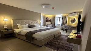 A hotel room with a large bed, bedside tables, a desk with a chair, and a wall-mounted TV. - Red Carpet Hotel & Suite (Amman)