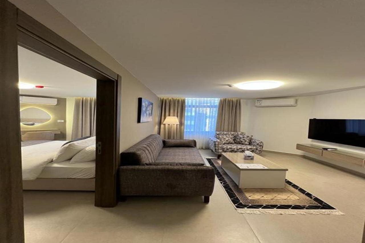 A modern hotel room with a bed, a sofa, a coffee table, and a TV.