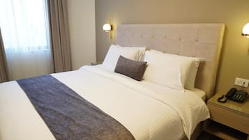A hotel room with a large bed, a bedside telephone, and a window with curtains.