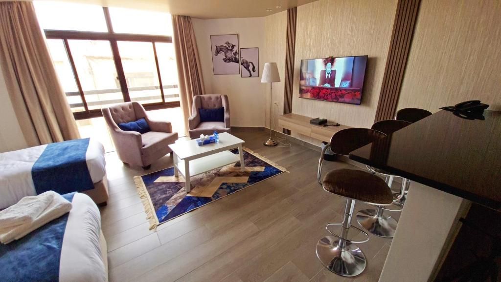 A hotel room with a bed, two armchairs, a coffee table, a TV, and a bar area.