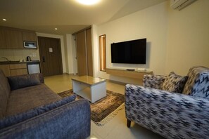 A living room with a sofa, a coffee table, and a television mounted on the wall. - Red Carpet Hotel & Suite (Amman)