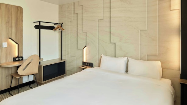 A hotel room with a bed, a desk with a chair, a coat rack, and a wall-mounted light fixture. - B&B Hotel Meaux Nanteuil-les-meaux (Nanteuil-les-Meaux)