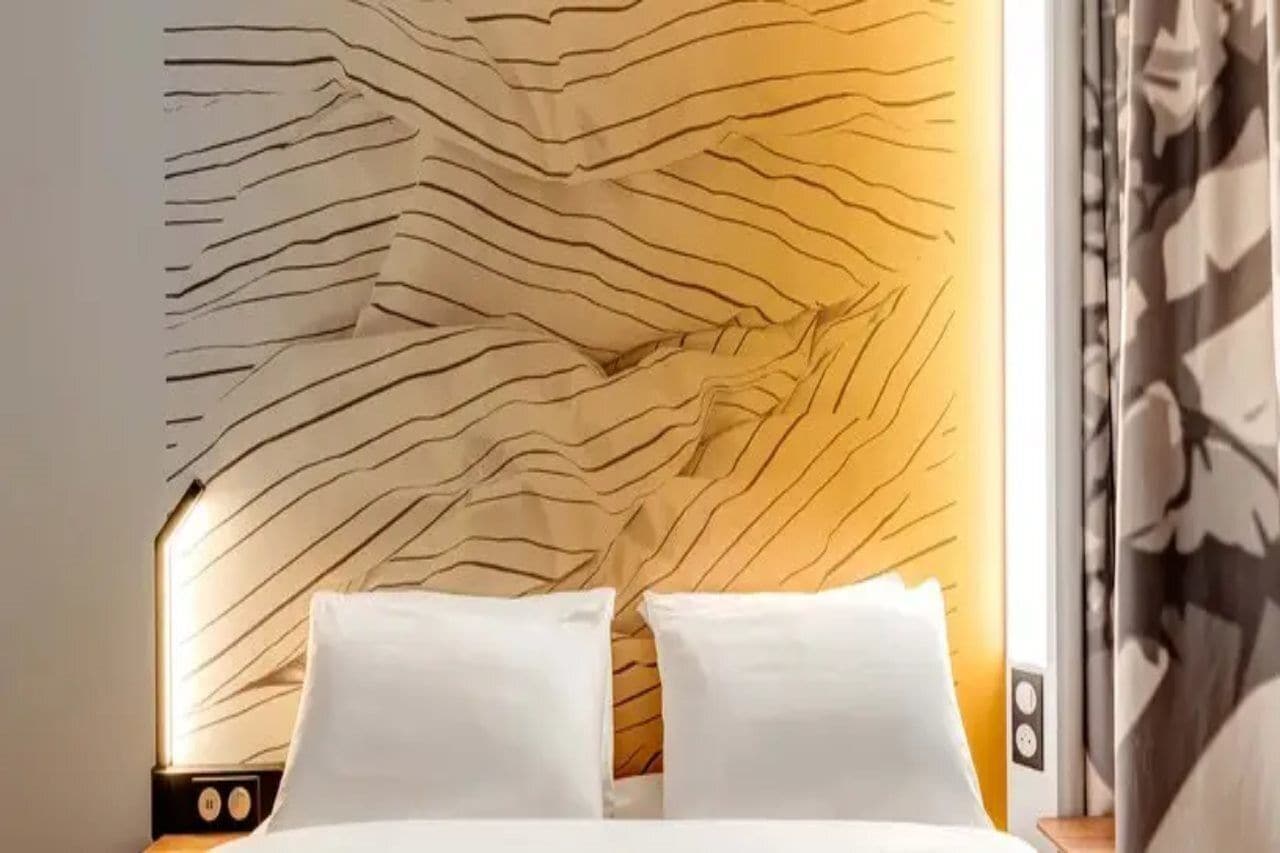 Un lit avec du linge de lit blanc et une tête de lit ornée d’un motif ondulé.