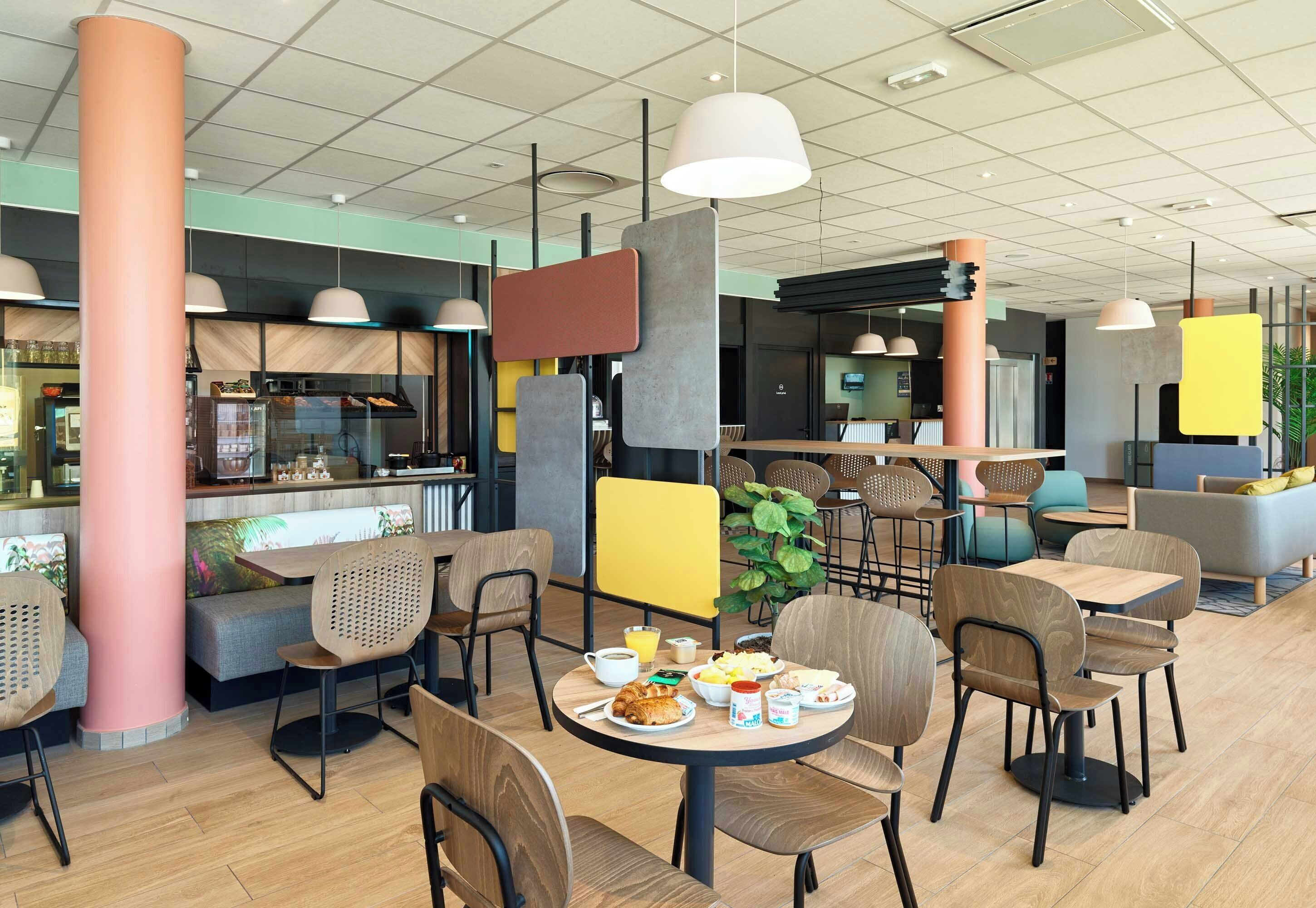 L’intérieur d’un café moderne, avec des tables et des chaises en bois, et divers types de sièges, notamment un banc et des chaises hautes.