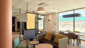 A modern lounge area with seating, tables, and large windows offering a view of the outside. - B&B Hotel Meaux Nanteuil-les-meaux (Nanteuil-les-Meaux)