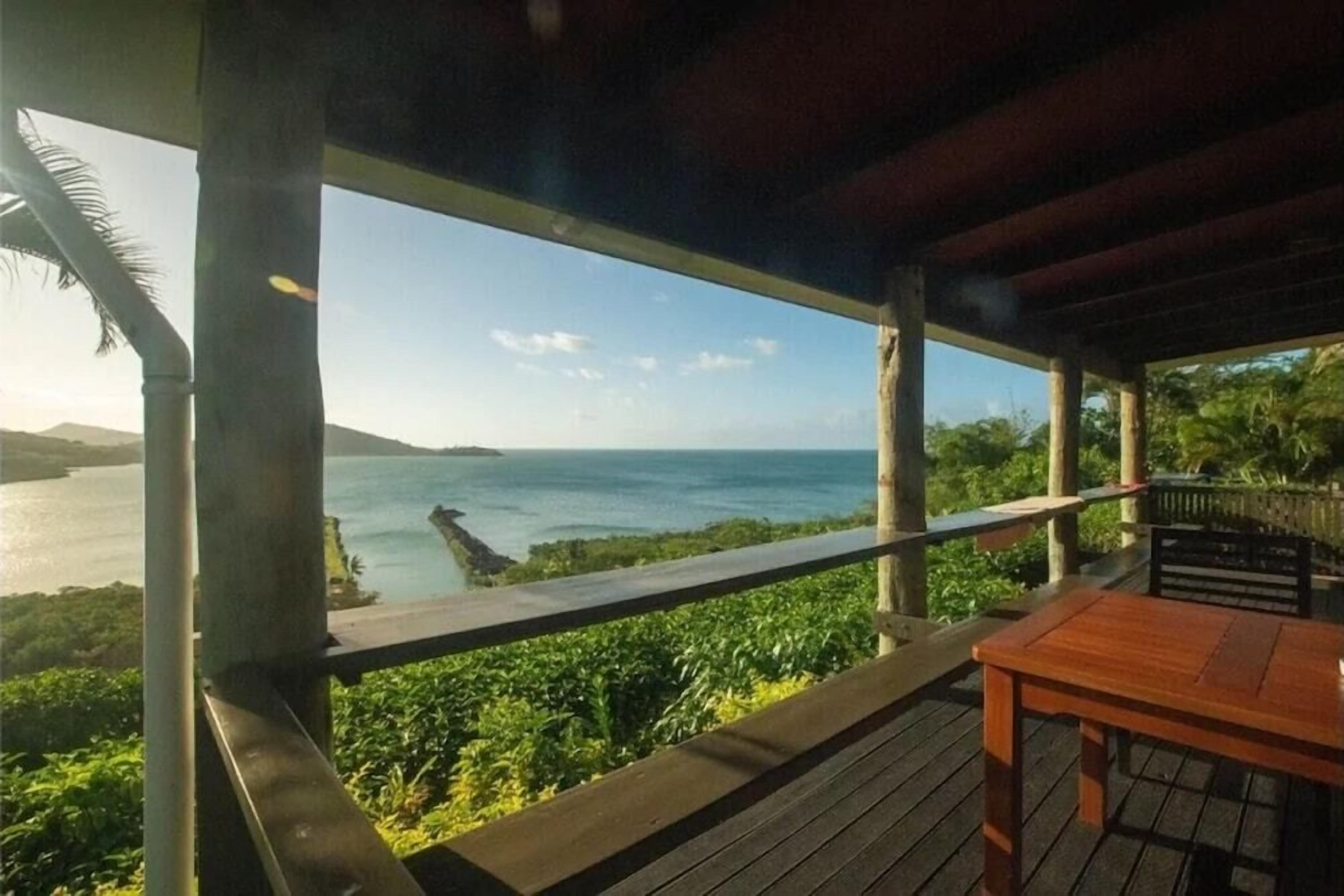 Una terraza de madera con una mesa y un banco, con vistas a un cuerpo de agua y vegetación.