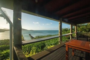 A wooden deck with a table and a bench, overlooking a body of water and greenery.