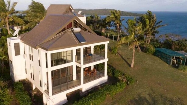 A modern two-story house with large windows and a balcony, surrounded by lush greenery and a view of the ocean. - Dreamview Villas (Rakiraki)