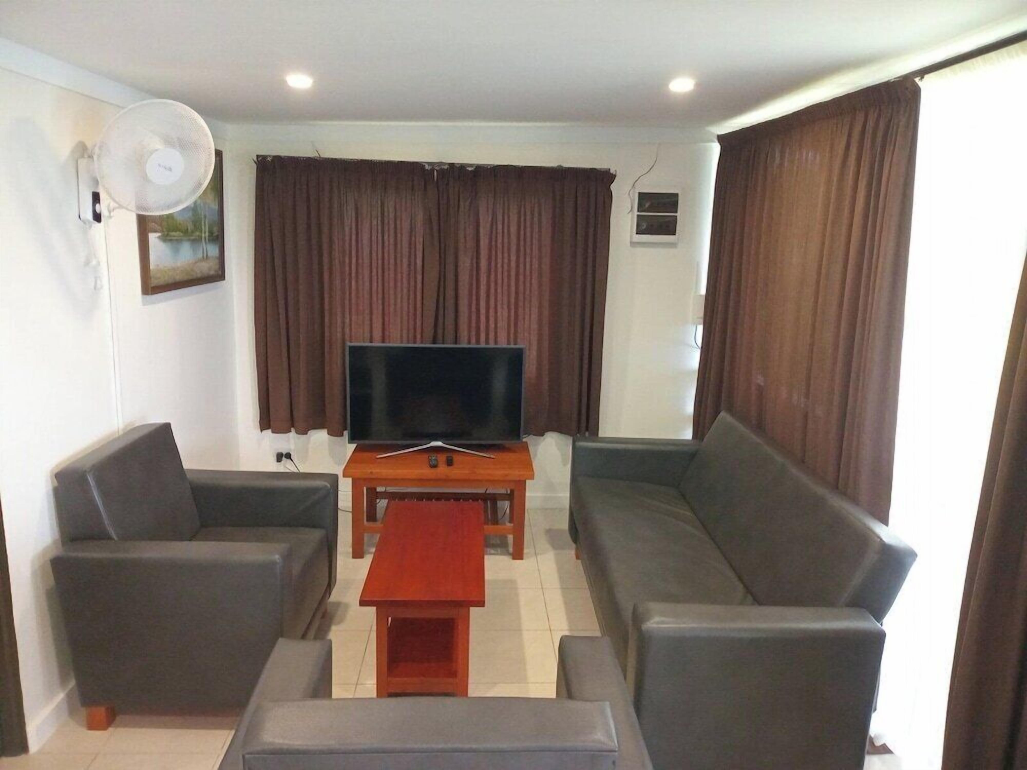 A living room with a flat-screen TV, a sofa, a coffee table, and a fan.